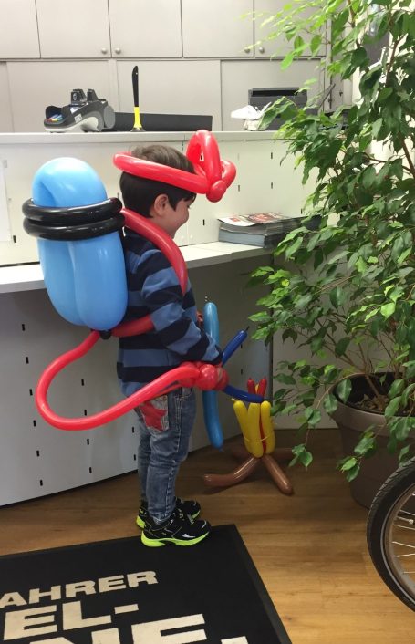 Kleines Kind mit einem Düsenrucksack und einem Helm aus Ballons.